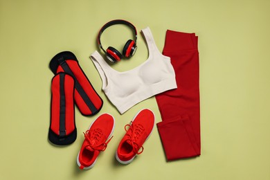 Photo of Sportswear, sneakers, headphones and ankle weights on pale olive background, flat lay
