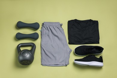 Photo of Sportswear, sneakers, dumbbells and kettlebell on pale olive background, flat lay