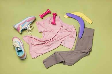 Photo of Sportswear, sneakers, dumbbells and boomerangs on pale olive background, flat lay
