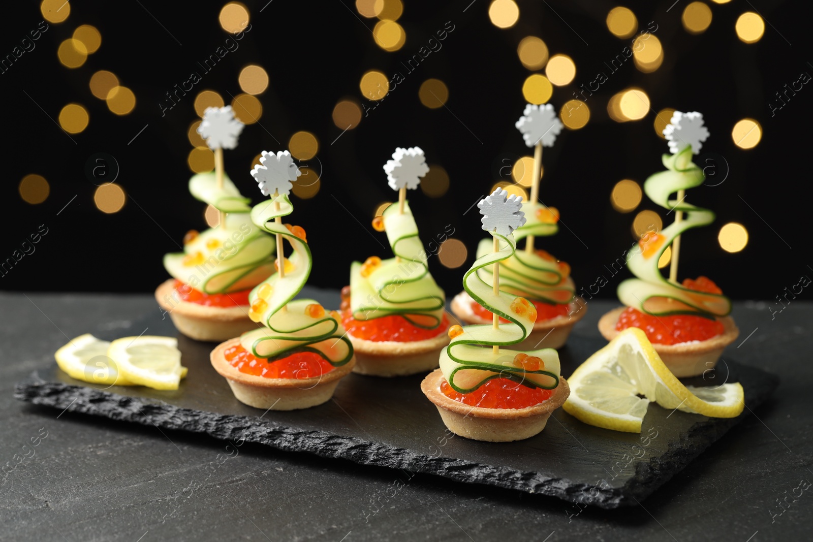 Photo of Tasty canapes on black table against dark background with blurred lights, closeup. Bokeh effect