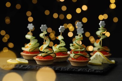 Photo of Tasty canapes on black table against dark background with blurred lights, closeup. Bokeh effect