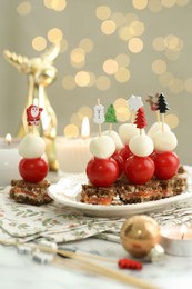 Photo of Tasty canapes and Christmas decor on white marble table against background with blurred lights, closeup. Bokeh effect