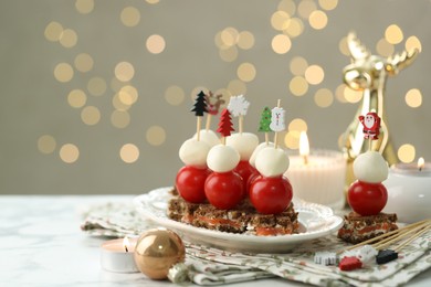 Photo of Tasty canapes and Christmas decor on white marble table against background with blurred lights, space for text. Bokeh effect