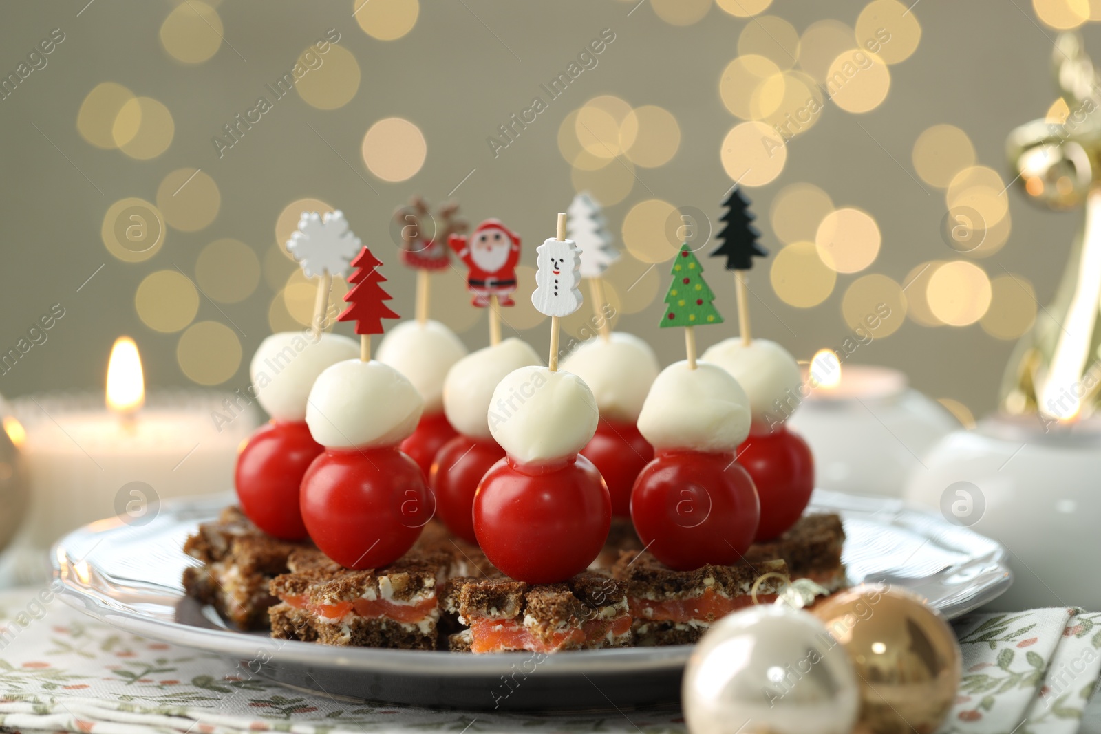 Photo of Tasty canapes and Christmas decor on table against background with blurred lights, closeup. Bokeh effect