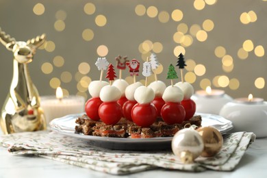 Photo of Tasty canapes and Christmas decor on white marble table against background with blurred lights, closeup. Bokeh effect
