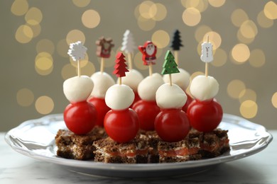 Photo of Tasty canapes on white marble table against background with blurred lights, closeup. Bokeh effect