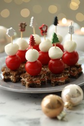 Photo of Tasty canapes and Christmas decor on white marble table against background with blurred lights, closeup. Bokeh effect