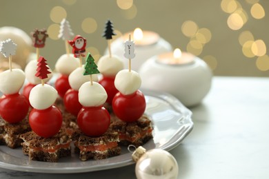 Photo of Tasty canapes and Christmas decor on white table against background with blurred lights, space for text. Bokeh effect