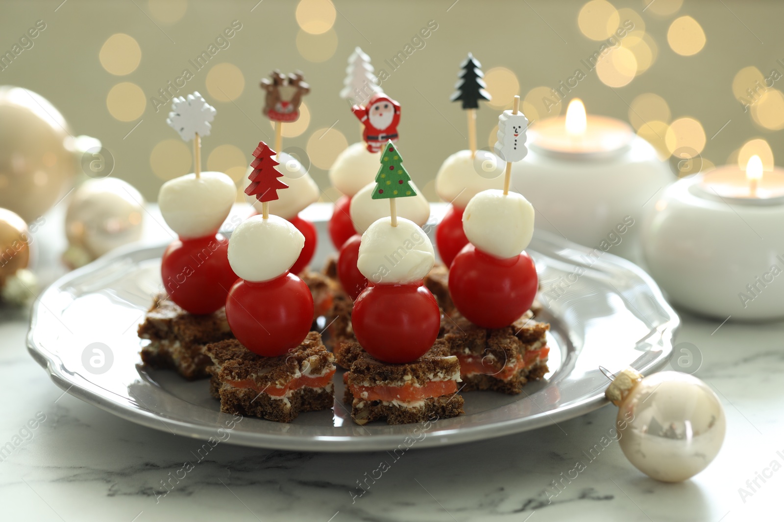 Photo of Tasty canapes and Christmas decor on white marble table against background with blurred lights, closeup. Bokeh effect