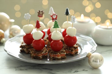 Photo of Tasty canapes and Christmas decor on white marble table against background with blurred lights, closeup. Bokeh effect