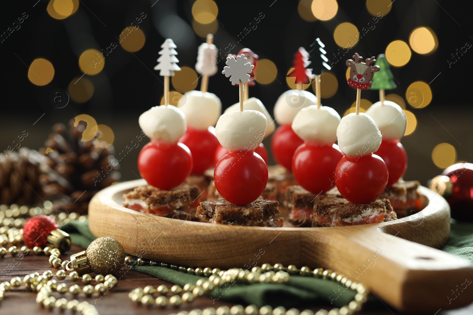 Photo of Tasty canapes and Christmas decor on wooden table against background with blurred lights, closeup. Bokeh effect