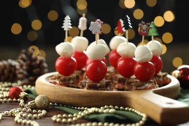 Photo of Tasty canapes and Christmas decor on wooden table against background with blurred lights, closeup. Bokeh effect