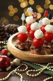 Photo of Tasty canapes and Christmas decor on wooden table against background with blurred lights, closeup. Bokeh effect