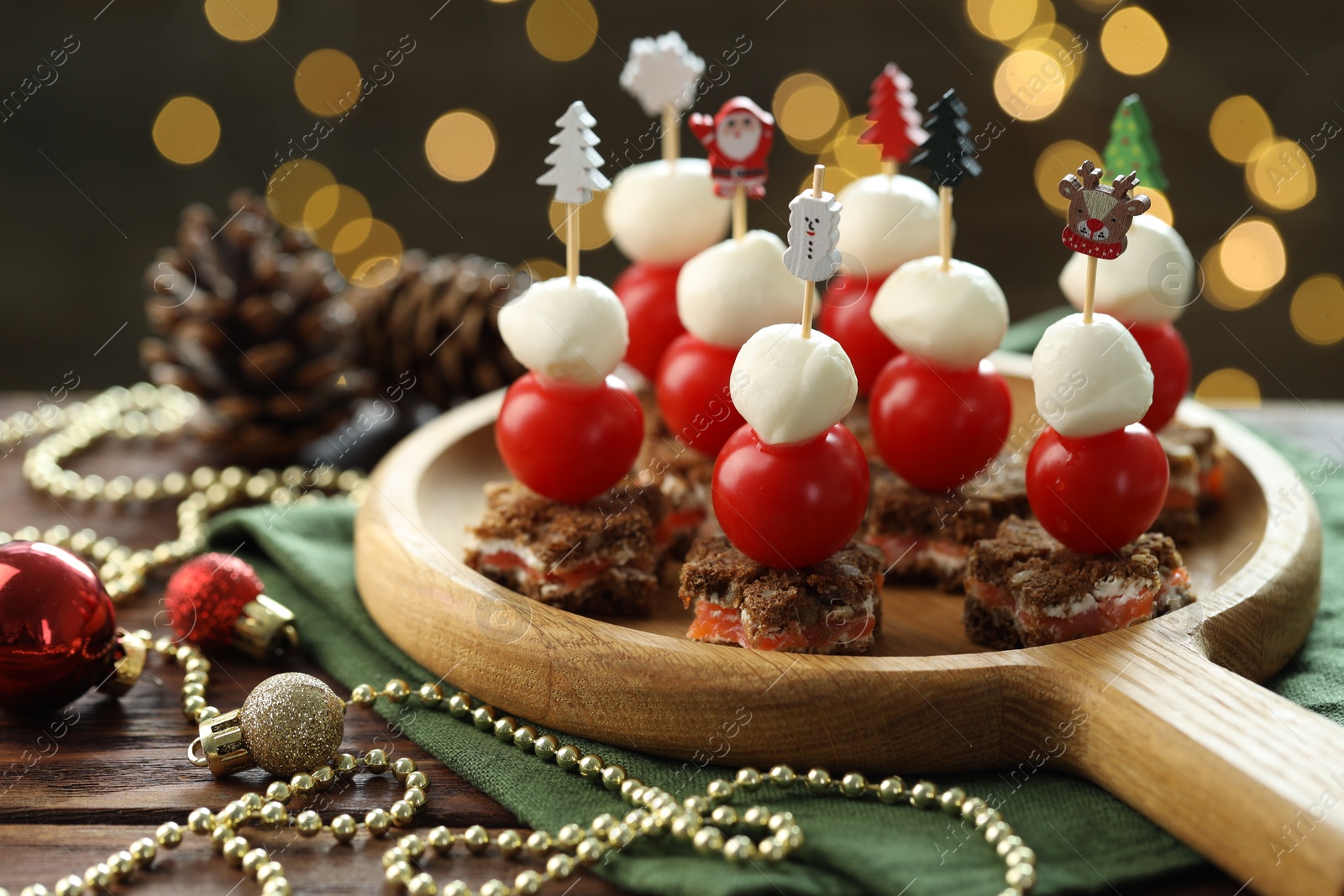 Photo of Tasty canapes and Christmas decor on wooden table against background with blurred lights, closeup. Bokeh effect