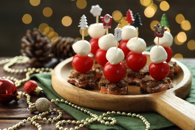 Photo of Tasty canapes and Christmas decor on wooden table against background with blurred lights, closeup. Bokeh effect