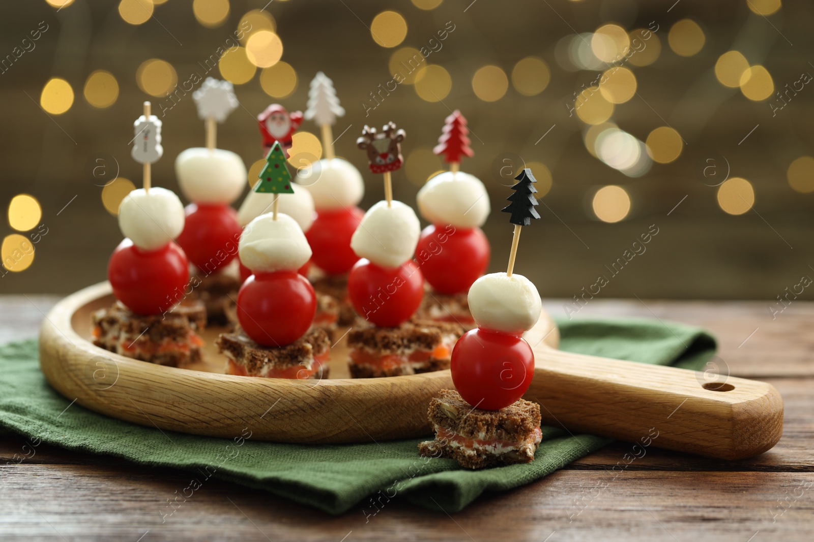 Photo of Tasty canapes on wooden table against background with blurred lights, closeup. Bokeh effect