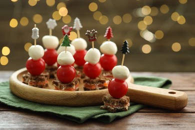 Photo of Tasty canapes on wooden table against background with blurred lights, closeup. Bokeh effect