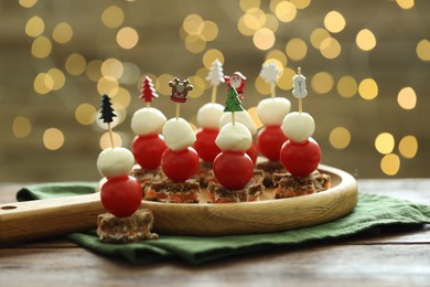 Photo of Tasty canapes on wooden table against background with blurred lights, closeup. Bokeh effect