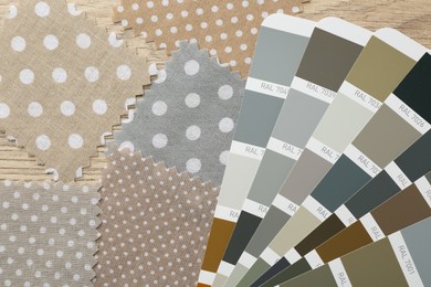 Photo of Samples of colorful fabrics and color palettes on wooden table, flat lay