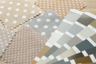 Photo of Samples of colorful fabrics and color palettes on wooden table, closeup