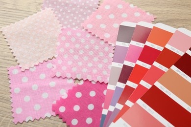 Photo of Samples of colorful fabrics and color palettes on wooden table, closeup