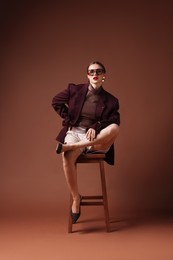 Photo of Young woman in stylish clothes on chair against brown background