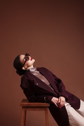 Photo of Young woman in stylish clothes on chair against brown background