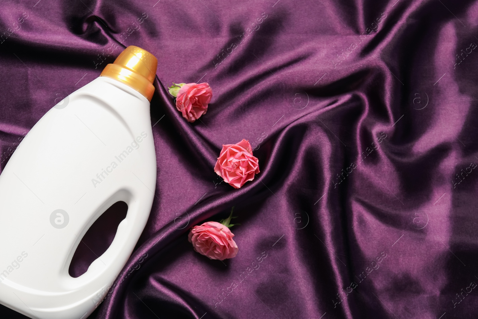 Bottle of fabric softener and flowers on purple cloth, flat lay. Space for text Photo of Bottle of fabric softener and flowers on purple cloth, flat lay. Space for text