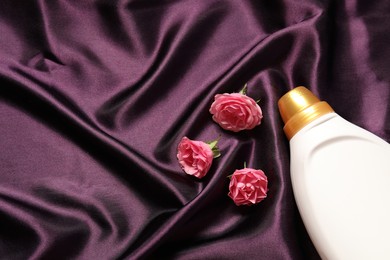 Photo of Bottle of fabric softener and flowers on purple cloth, flat lay. Space for text
