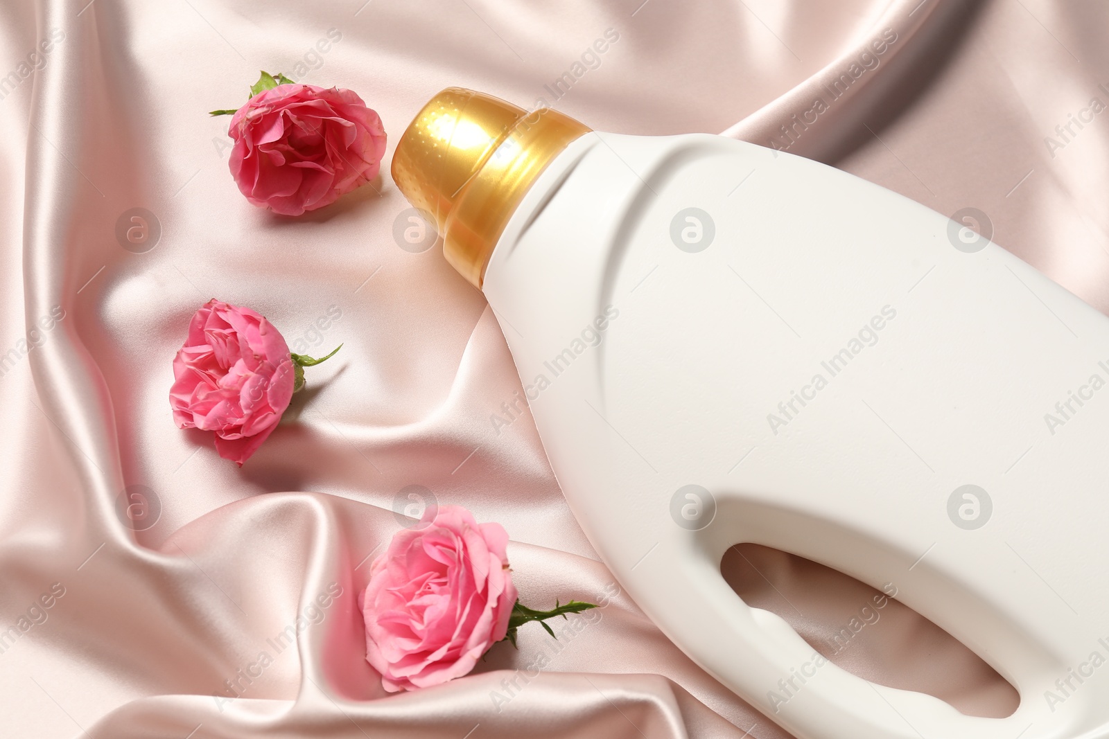 Photo of Bottle of fabric softener and flowers on beige cloth, above view