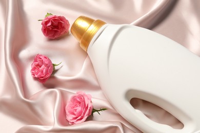 Photo of Bottle of fabric softener and flowers on beige cloth, above view