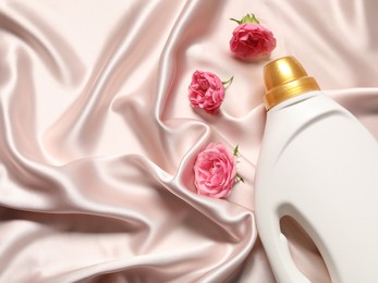 Photo of Bottle of fabric softener and flowers on beige cloth, flat lay. Space for text