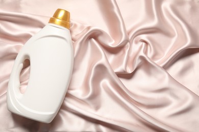 Photo of Bottle of fabric softener on beige cloth, top view. Space for text