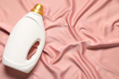 Photo of Bottle of fabric softener on pink cloth, top view. Space for text