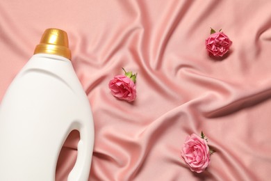 Photo of Bottle of fabric softener and flowers on pink cloth, flat lay