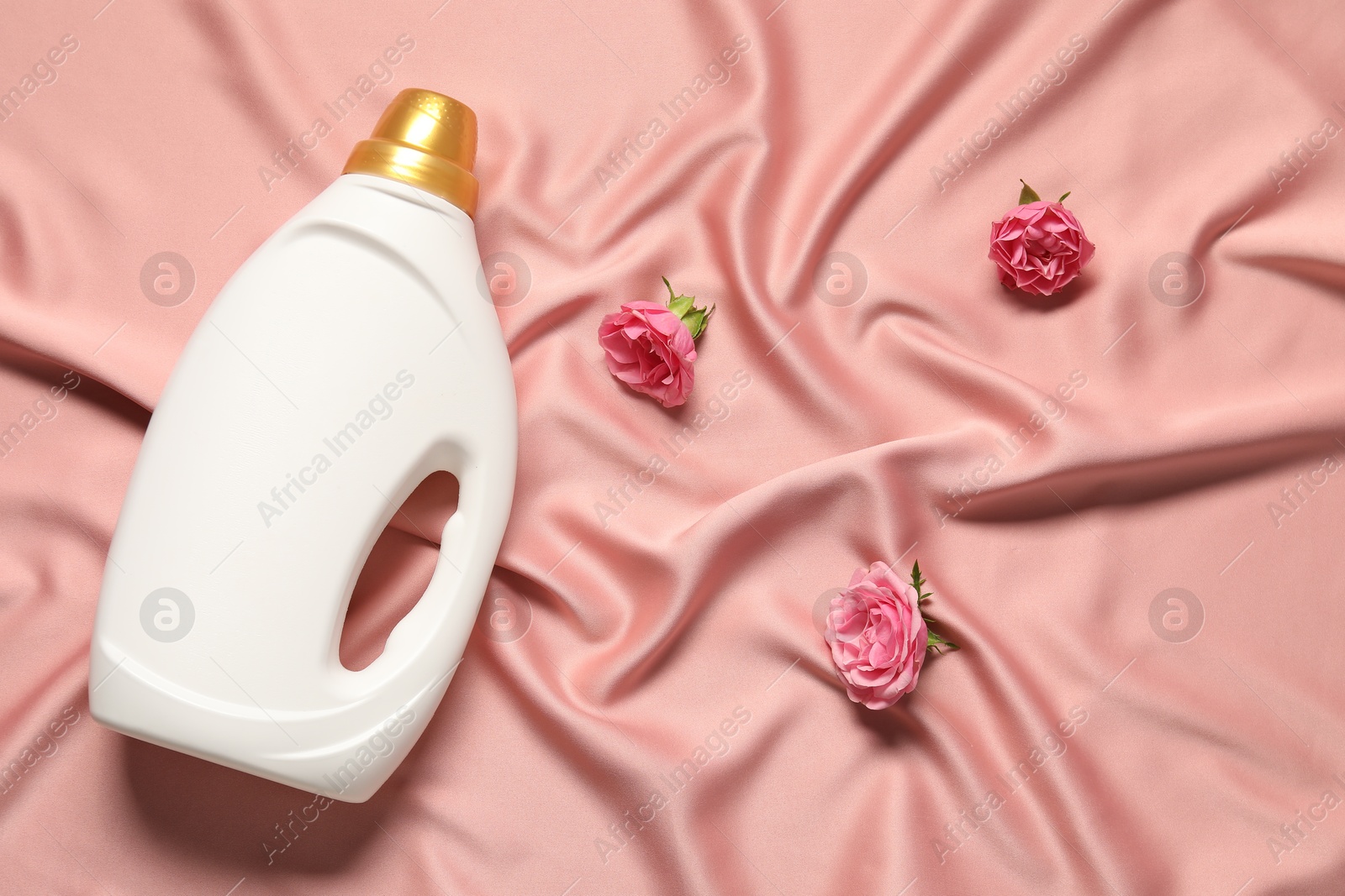 Bottle of fabric softener and flowers on pink cloth, flat lay Photo of Bottle of fabric softener and flowers on pink cloth, flat lay
