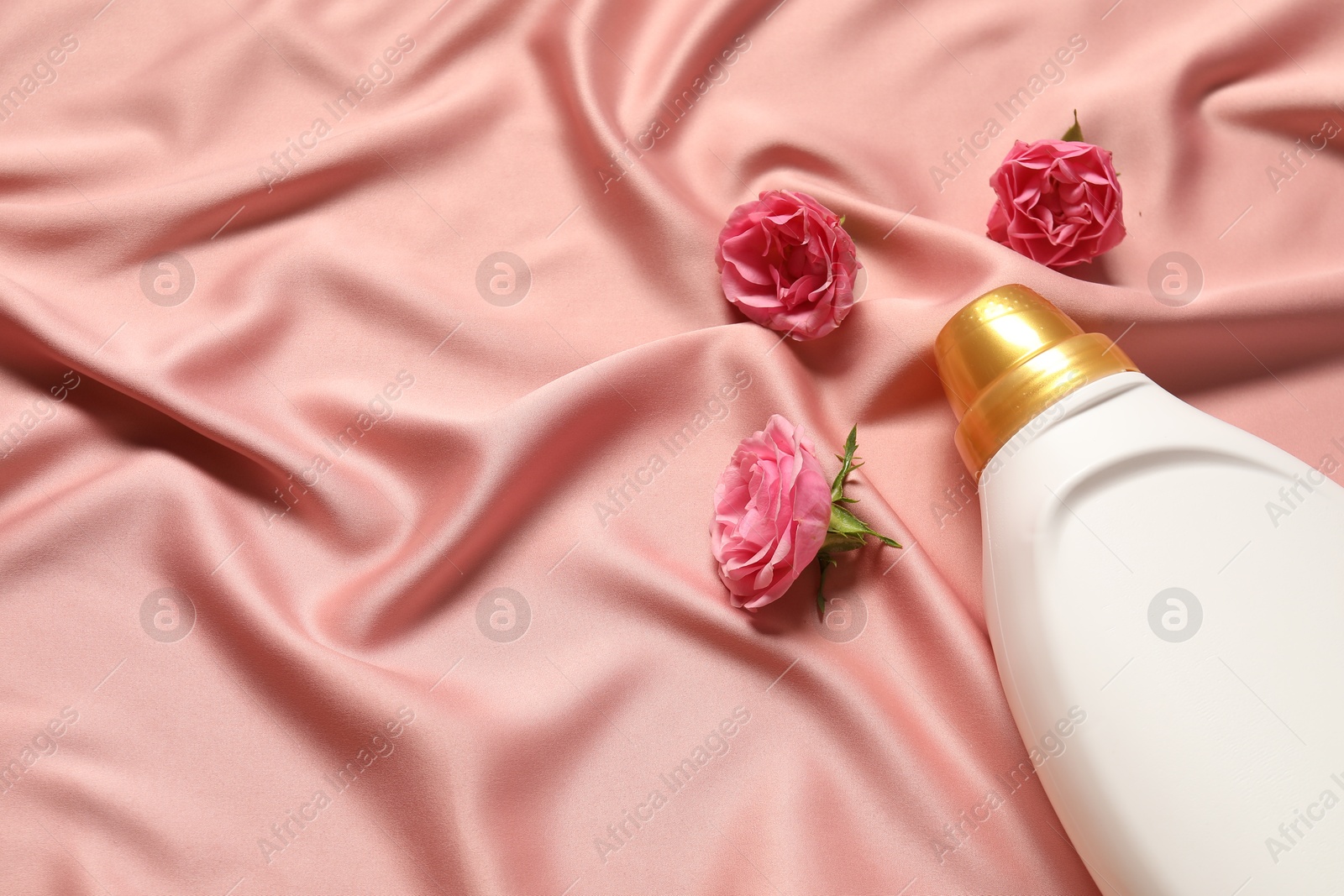 Photo of Bottle of fabric softener and flowers on pink cloth, above view. Space for text