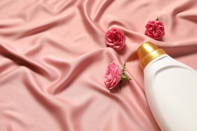 Photo of Bottle of fabric softener and flowers on pink cloth, above view. Space for text