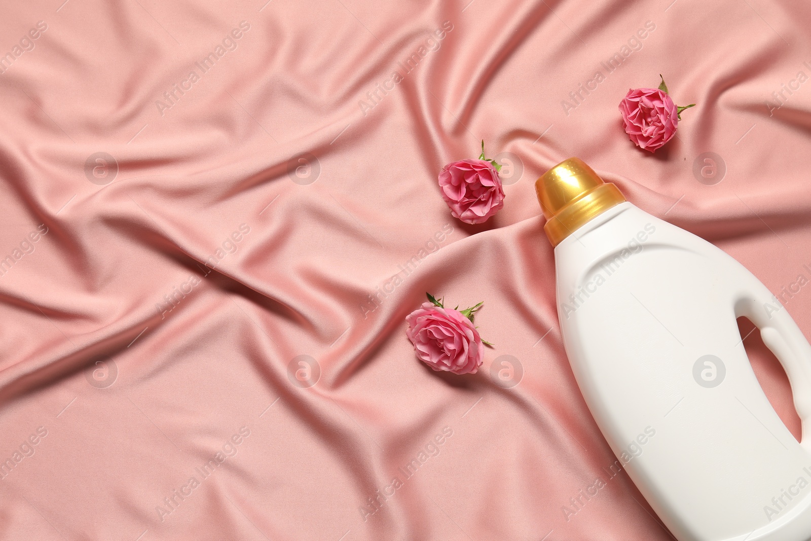Photo of Bottle of fabric softener and flowers on pink cloth, flat lay. Space for text