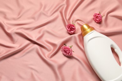 Photo of Bottle of fabric softener and flowers on pink cloth, flat lay. Space for text