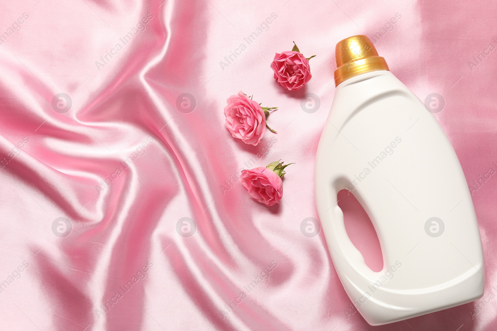 Photo of Bottle of fabric softener and flowers on pink cloth, flat lay. Space for text