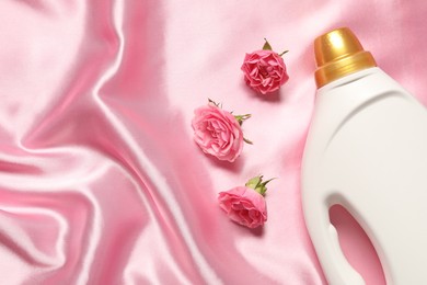 Photo of Bottle of fabric softener and flowers on pink cloth, flat lay. Space for text