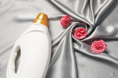 Photo of Bottle of fabric softener and flowers on grey cloth, flat lay