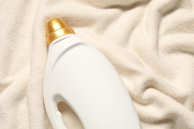 Photo of Bottle of fabric softener on soft cloth, top view