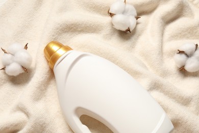 Photo of Bottle of fabric softener and cotton flowers on soft cloth, flat lay