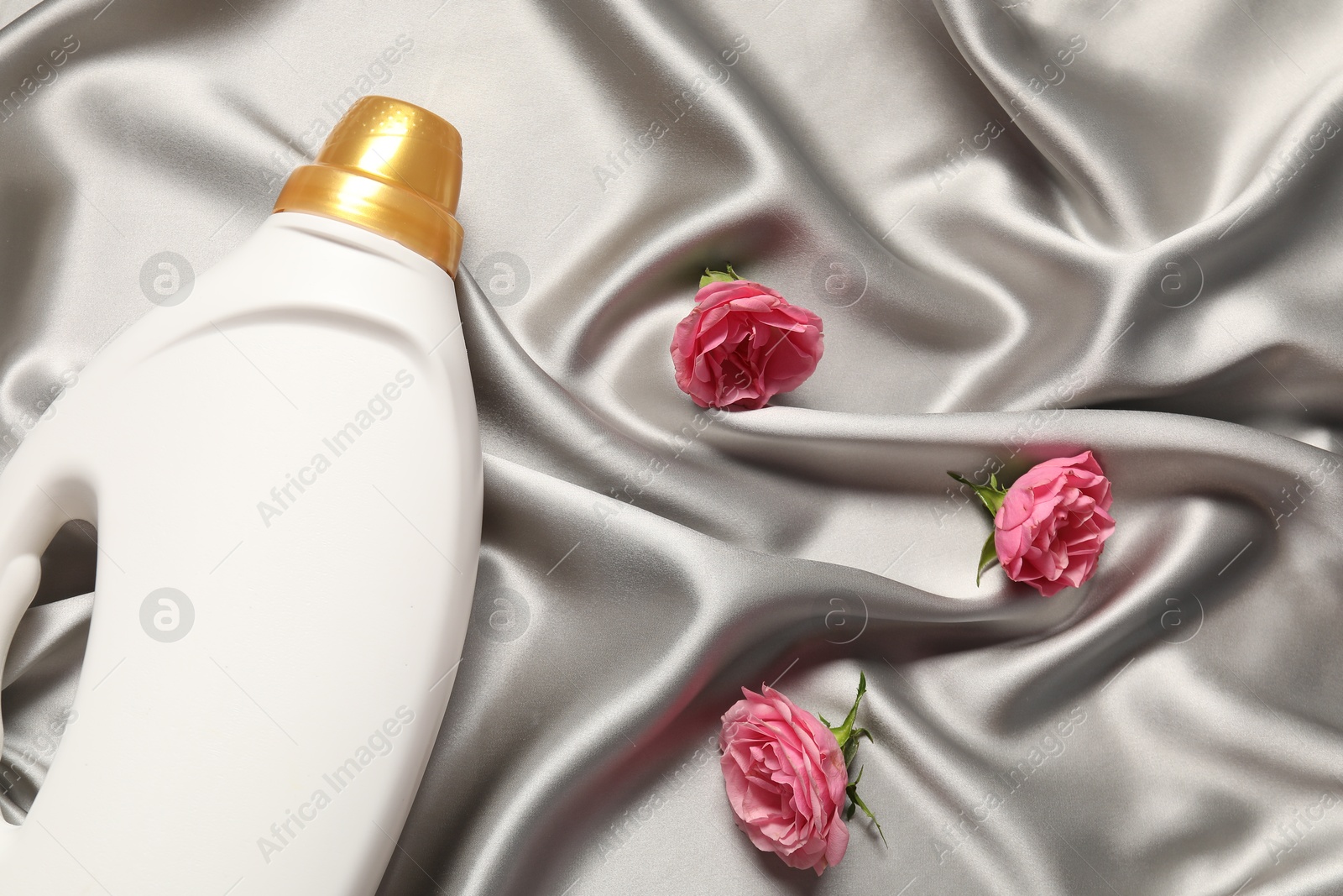 Photo of Bottle of fabric softener and flowers on grey cloth, flat lay
