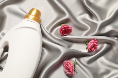 Photo of Bottle of fabric softener and flowers on grey cloth, flat lay