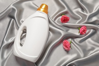 Photo of Bottle of fabric softener and flowers on grey cloth, flat lay