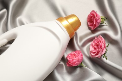 Photo of Bottle of fabric softener and flowers on grey cloth, above view