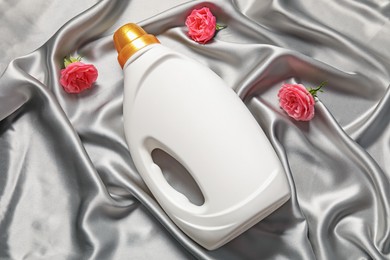 Photo of Bottle of fabric softener and flowers on grey cloth, flat lay